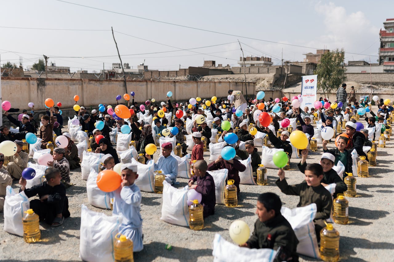 Children gather with balloons and supplies during a daytime event in Afghanistan.